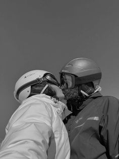 two people with helmets on their heads standing next to each other and one person is kissing the other