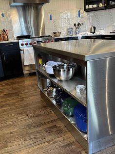 a kitchen with stainless steel appliances and wooden flooring is pictured in this image, there are bowls on the bottom shelf