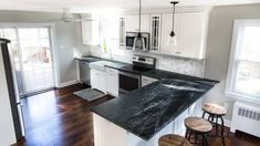 a kitchen with white cabinets and black counter tops, hardwood floors, and stainless steel appliances