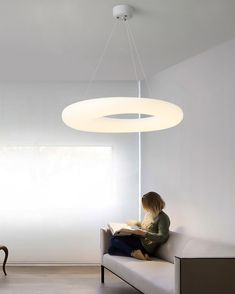 a woman sitting on a couch reading a book under a light fixture in a living room