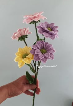 crocheted flowers are being held in the palm of someone's hand on a gray background