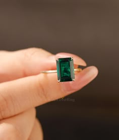 a woman's hand holding an emerald ring