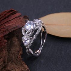 a white gold ring with three stones on top and a leaf in the middle, sitting next to it