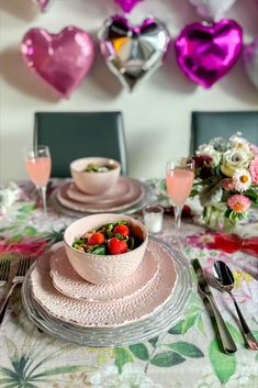 the table is set with pink plates, silverware and heart - shaped balloons in the background