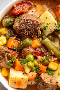 a bowl filled with meat, vegetables and potatoes on top of a white tablecloth