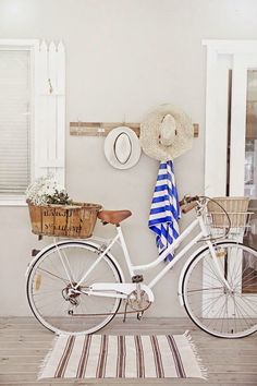 a white bicycle parked next to a wall with a hat on it's rack