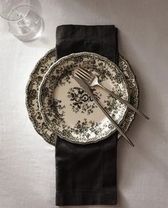 a table setting with black and white plates, silverware and wine glasses on it