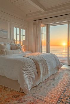 a large bed sitting in a bedroom next to an open window with the sun setting