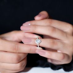 a woman's hands holding a ring with a heart shaped diamond on it,