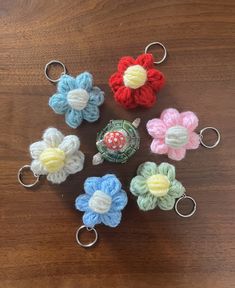 six crocheted flower keychains on a wooden table with one being held in the middle