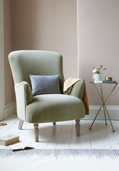 a green chair sitting next to a small table with flowers on it and a blue pillow