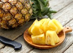 sliced pineapple on a wooden plate next to a knife