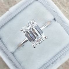 an emerald - cut diamond ring sits in a velvet box on top of a carpeted surface