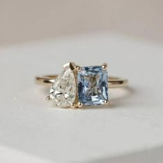 an engagement ring with two pear shaped blue and white diamonds on the sides, set in yellow gold