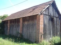 an old brick building sitting on the side of a road next to tall grass and trees