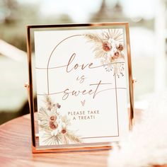 a sign that says love is sweet on top of a wooden table with feathers around it