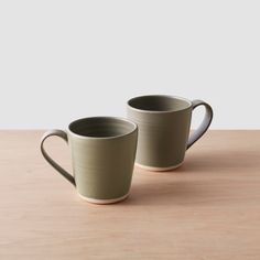 two coffee mugs sitting on top of a wooden table next to eachother