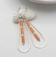 Rev up your style with our Harley hoop earrings. Made of durable sterling silver, these boho-inspired hoops feature fiery orange Miyuki seed beads for a pop of color. Perfect for adding some edge to any outfit. Approximately 2.25” long Made with .925 Sterling Silver Quality Translucent Orange Miyuki Seed Beads Polished to a high shine Handmade in Montana Sent in a ribboned gift box with polishing cloth Orange Beaded Hoop Earrings, Elegant Orange Nickel-free Earrings, Nickel-free Orange Beaded Dangle Earrings, Nickel-free Orange Hoop Earrings, Orange Nickel-free Bohemian Hoop Earrings, Earring Inspo, African Turquoise, Wire Work Jewelry, Work Jewelry