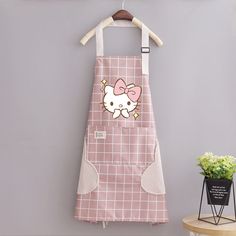 a hello kitty kitchen apron hanging on a wall next to a potted plant and small vase