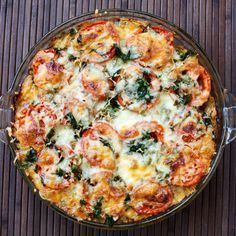 a casserole dish with tomatoes, spinach and cheese in it on a wooden table