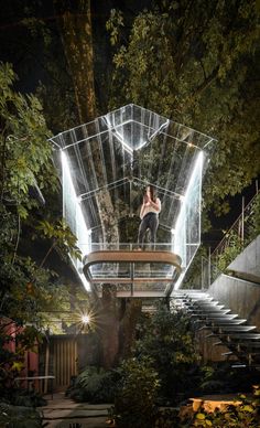 a woman standing on top of a glass structure in the middle of some trees at night