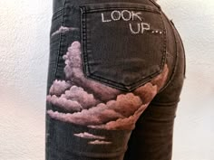 the back of a woman's jeans with clouds painted on it and words that read look up