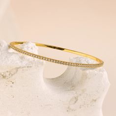 Our Classic Diamond Tennis Bangle is a dainty gold piece adorned with sparkling pavé stones, exuding elegance and sophistication. Perfect for any occasion, this versatile bracelet can be worn alone for a subtle touch of glamour or stacked with other bracelets for a classy, layered look ♡ SKU: RR-BR065 Product Details Material: 18K Gold Over Brass Finish: 18K Gold Featuring ~2.5mm wide Diamond Bangle Bracelet with CZ Pavé Diamond Stones Featured Styles Part of our Diamond & Pavé Collection Model