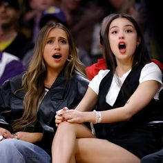 two young women sitting next to each other at a basketball game, one with her mouth open