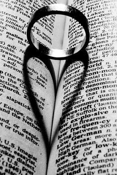 a heart shaped shadow on top of an open book with a ring in the middle