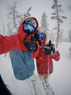 two people on skis in the snow wearing goggles and holding their arms out