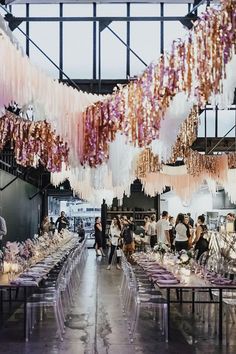 people are standing around tables with purple and white decorations hanging from the ceiling above them