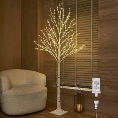 a living room with a white chair and a lighted tree next to a window in the corner