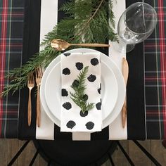 the place setting is set with black and white napkins, silverware, and evergreen branches