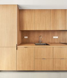 an empty kitchen with wooden cabinets and a sink in the center is seen from across the room