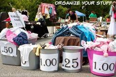 several buckets filled with clothes sitting on the ground next to a sign that says how to sell your stuff at a garage sale