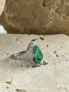 an emerald and diamond ring sitting on top of a rock