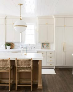 a kitchen with white cabinets and an island in the center, two wicker chairs at the end