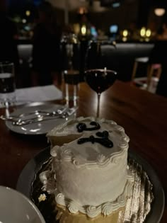 a white cake sitting on top of a table next to a glass of red wine