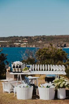 an outdoor table set up with wine glasses and plates on it, next to the ocean