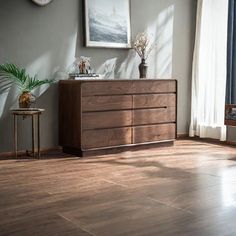 a wooden dresser sitting in front of a window next to a potted plant on a table