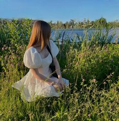 a woman sitting in tall grass next to a body of water