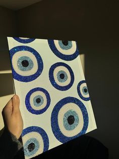 a person holding up an art piece with blue and white circles on it