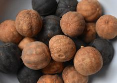 a white bowl filled with lots of brown and black fruit next to each other on top of a table