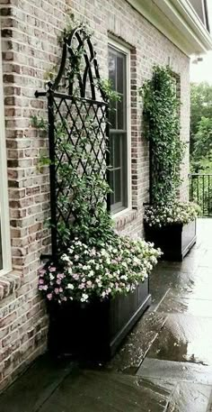 two black planters filled with flowers next to a brick building on a rainy day