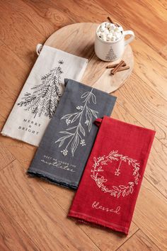 three tea towels on a wooden tray next to a cup of hot chocolate and marshmallows