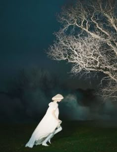 a woman standing in front of a tree at night wearing a white dress and hat