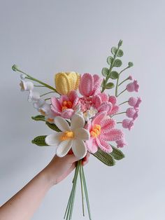 a hand holding a crocheted flower bouquet in pink, yellow and white colors