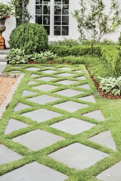 a stone walkway in front of a house with grass growing on the ground and bushes around it