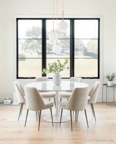 a dining room table with six chairs and a vase on the top, in front of two large windows