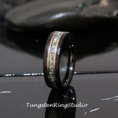 a wedding band with green moss inlays on the inside of it, sitting on top of a shiny surface